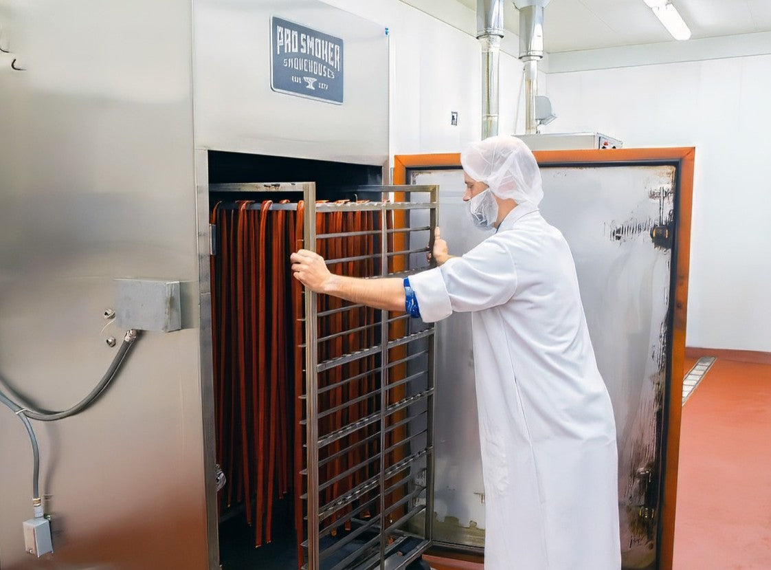 Person in a white coat and hairnet operating a large industrial oven in a factory setting.