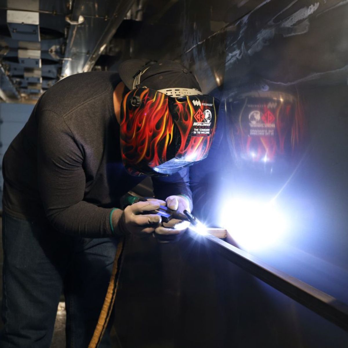 Person welding a vehicle with a helmet featuring flames.