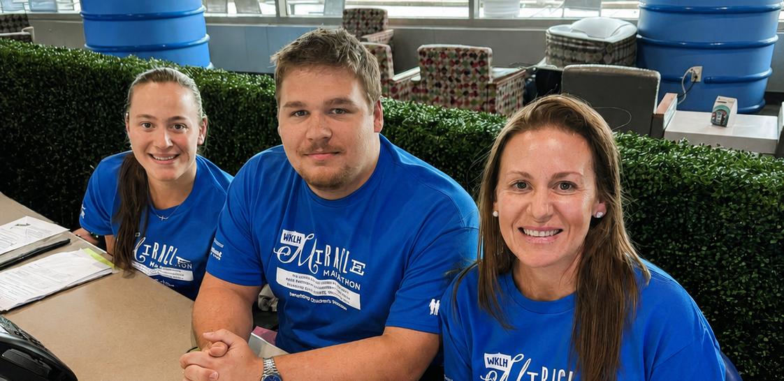 Three people wearing blue shirts with a logo sitting at a table in an office setting.